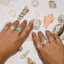 Two hands wearing rings on a background of seashells