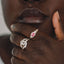 Close-up of a hand wearing a silver ring with a pink gemstone, held near the face.