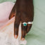 Hand wearing a silver ring with a green gemstone on a shell against a light green background