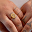 Close-up of a hand wearing a gold ring with a circular design on a plain background
