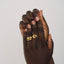 Hand wearing a gold ring with a green gemstone on a plain background